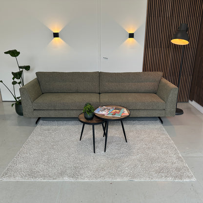 Groen gemêleerde 4-zitsbank Zoë van INNO living met strakke belijning en comfortabele zit, opgesteld in een lichte showroom met vloerkleed en tafeltjes.