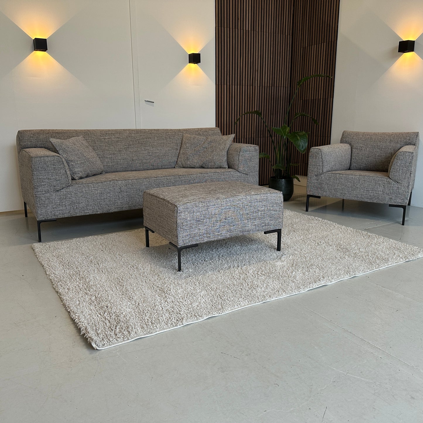 Gemêleerde Design on Stock Bloq zithoek met rechte bank, fauteuil en hocker, strakke lijnen en stevige kussens, opgesteld in een lichte showroom.