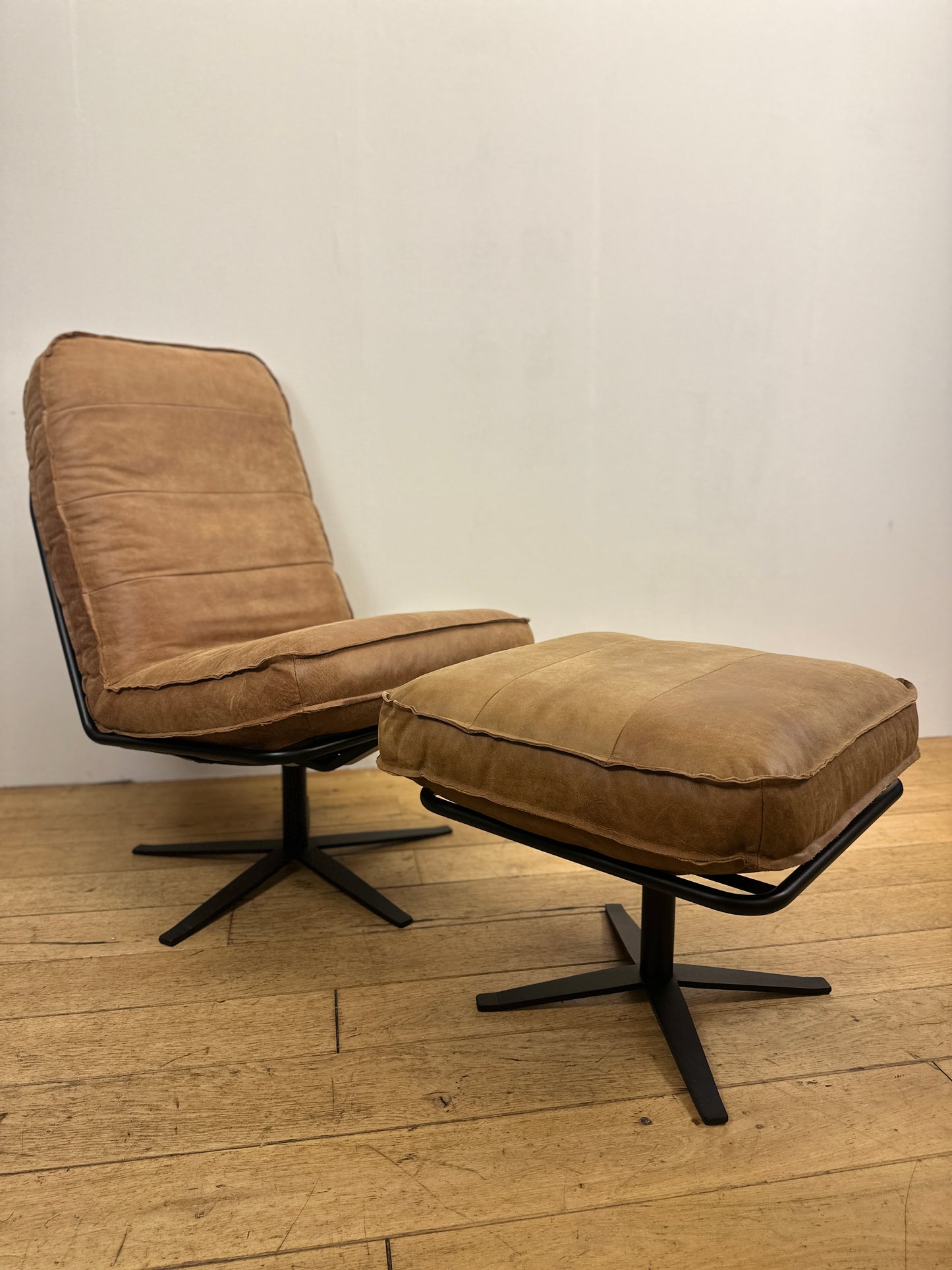 Cognackleurige leren fauteuil Odin van INNO living met bijpassende voetenbank, comfortabel gevormde zitting en zwart metalen onderstel op houten vloer.