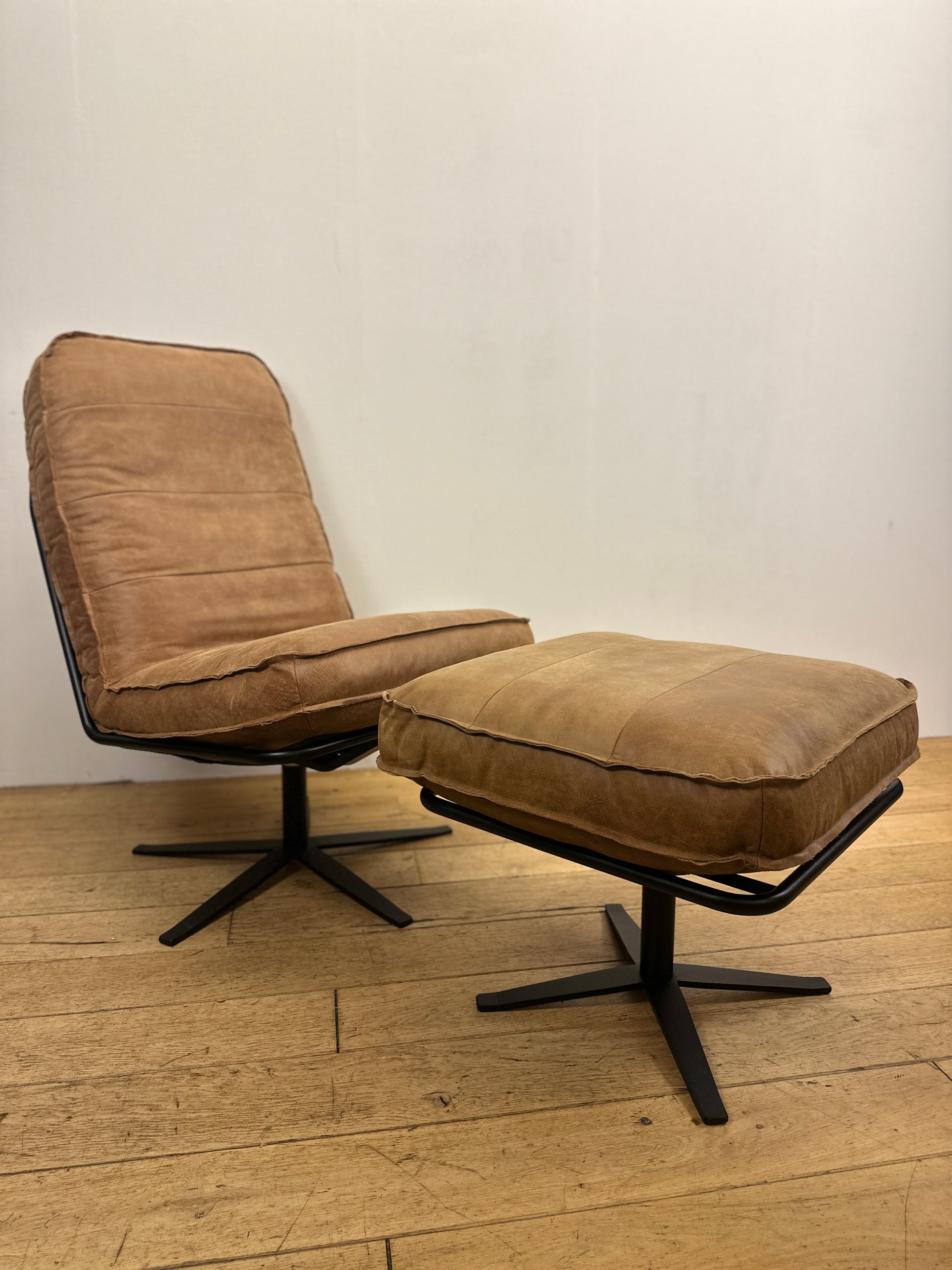 Cognackleurige leren fauteuil Odin van INNO living met bijpassende voetenbank, comfortabel gevormde zitting en zwart metalen onderstel op houten vloer.